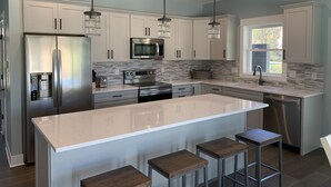 A modern kitchen with stainless steel appliances, a large island with stools, and pendant lighting. - Beautiful newer construction 2021 home in town! (Saugatuck)