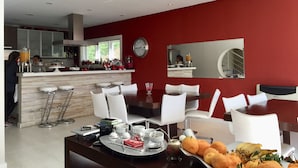 A modern kitchen with a red accent wall, a dining area with white chairs, and a bar with stools. - Wonderful house in Campos do Jordão  (SP)