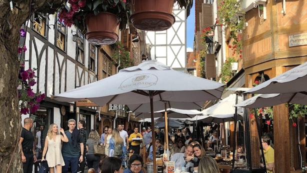 An outdoor café with wooden tables and chairs, surrounded by buildings with flower boxes and hanging pots. - Wonderful house in Campos do Jordão  (SP)
