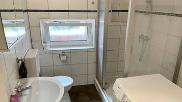 A bathroom with a toilet, sink, shower, and a window.