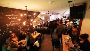 Un espace bar/salon avec des tables, des chaises et un mur en briques orné d’enseignes.