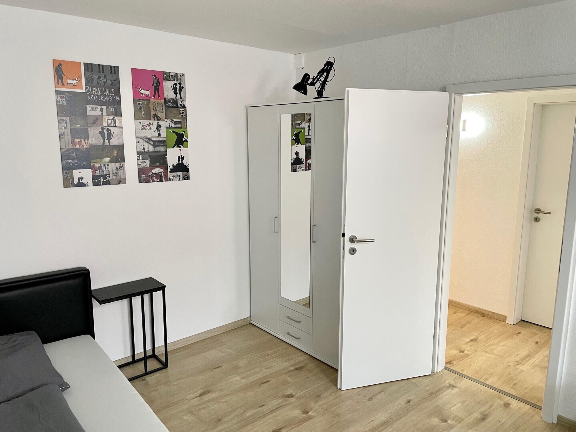 A room with a bed, a desk, a wardrobe, and a door leading to another room.