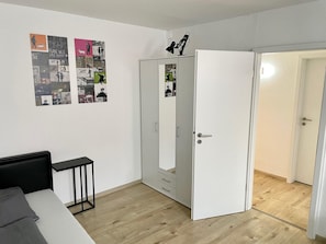 Une pièce comprenant un lit, un bureau, une armoire et une porte donnant sur une autre pièce.
