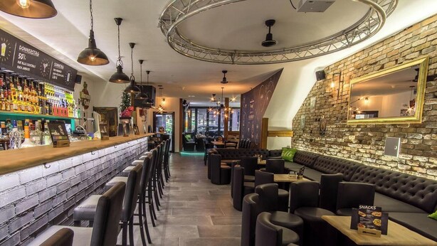 Un espace bar avec un mur en briques, des tabourets de bar et un comptoir où sont exposées différentes bouteilles.