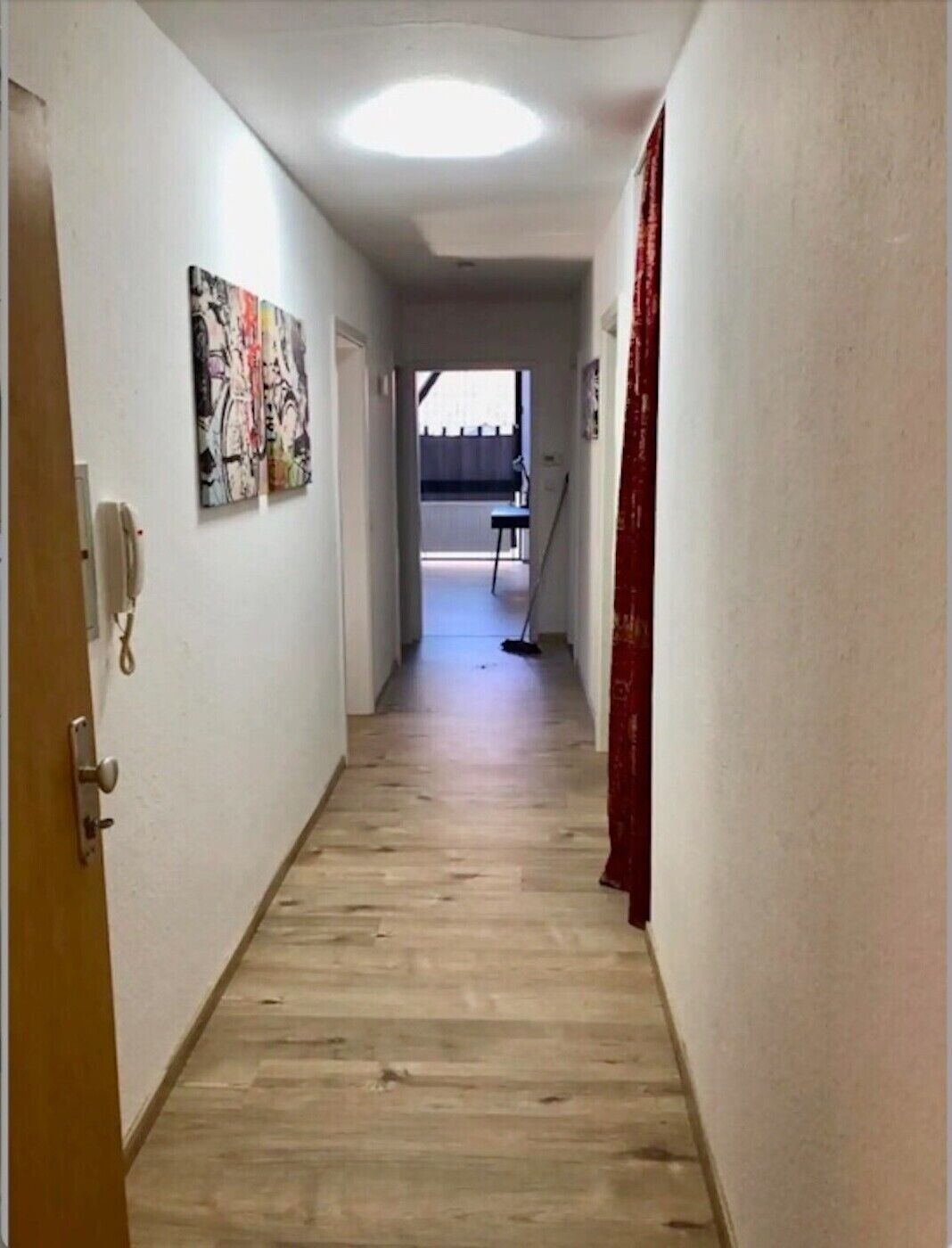 Ein Flur mit Holzboden, einer Tür links und einem roten Vorhang rechts.