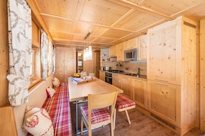 Ein Holzinterieur mit Küchenzeile, einem Esstisch mit Stühlen und einer Bank mit Kissen.