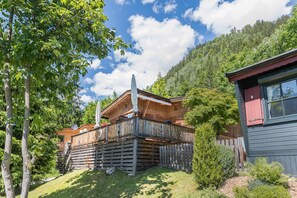 Une cabane en bois dotée d’un balcon, entourée d’arbres et avec une chaîne de montagnes en toile de fond.