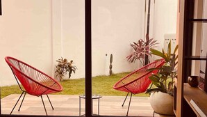 A view from inside a room with two red chairs facing a small outdoor area with grass and plants. - Immaculate 2-Bed Apartment at PamV Estates Apt6 (Accra)