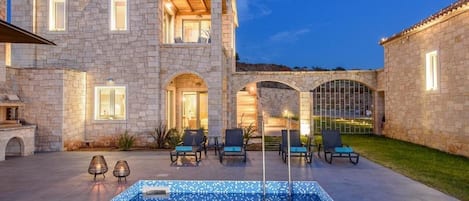 A stone building with a swimming pool, outdoor seating, and a covered patio area.