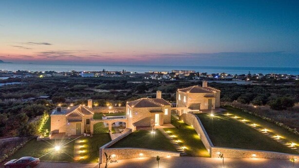 A stone villa with a courtyard, surrounded by a landscaped garden and a view of the sea at dusk. - Caldera Theros Villas (Hersonissos)