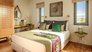 A bedroom with a bed, bedside tables, a desk, a mirror, and large windows. - Caldera Theros Villas (Hersonissos)