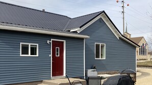 A blue single-story house with a red door, a small window, and a covered outdoor table and chairs.