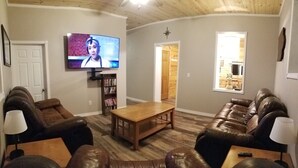 A living room with a wooden ceiling, a television mounted on the wall, a bookshelf, and leather sofas.