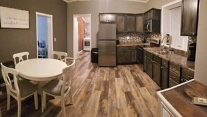 A modern kitchen with dark wood cabinets, a stainless steel refrigerator, and a dining area with a round table and chairs.
