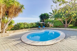 Una piscina circular con solárium empedrado, rodeada de exuberante vegetación y algunas sillas de descanso.