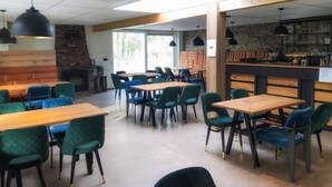 A modern restaurant with wooden tables and green chairs, a brick wall, and a bar area with glasses. - De Brenkberg by Interhome (Schinveld)