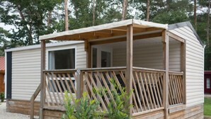 A wooden cabin with a porch and a small deck, surrounded by trees and a gravel ground. - De Brenkberg by Interhome (Schinveld)