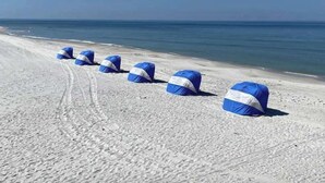A beach with several blue and white beach umbrellas lined up along the shore.