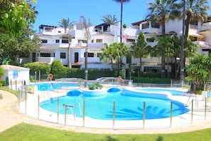 Une piscine entourée d’une terrasse, de palmiers et, au loin, d’un immeuble à plusieurs étages.