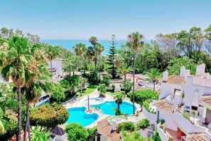 Ein Resort mit einem zentral gelegenen Schwimmbad, umgeben von Palmen und Blick aufs Meer.