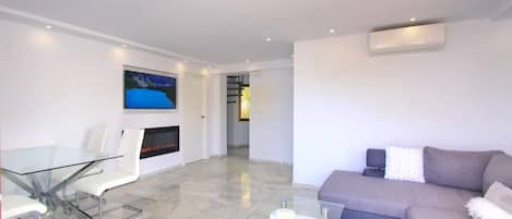 Un salon moderne avec une table basse en verre, un canapé, un téléviseur à écran plat et une cheminée.
