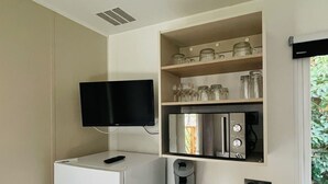 Een compacte keuken met een ingebouwde koelkast, een koffieapparaat en een flatscreen televisie boven de aanrecht.