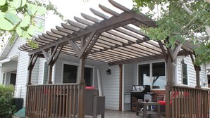 Een overdekt terras met een houten pergola, tuinmeubilair en een barbecuehoek.