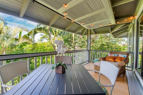 A covered outdoor area with a table and chairs, surrounded by lush greenery and a view of the sky. - Executive Family 4BR Princeville Home by beaches & the park w/AC, SPA and Bikes (Princeville)