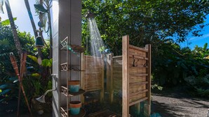 A wooden structure with a showerhead, surrounded by plants and a gravel path.