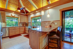 A modern kitchen with wooden cabinets, a central island, and pendant lighting. - Executive Family 4BR Princeville Home by beaches & the park w/AC, SPA and Bikes (Princeville)