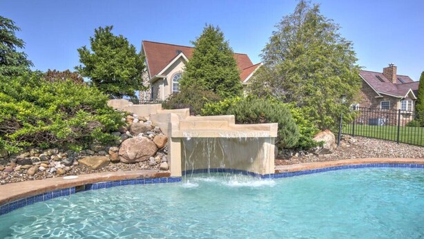 A swimming pool with a waterfall feature, surrounded by a stone border and a pebble bed.