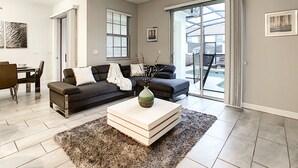 A modern living room with a dark sofa, a white coffee table, and a view of a pool through large glass doors. - 4BR 3BA, Access 2 Waterparks, Private Pool, FREE Grill. Near Disney Orlando! (Davenport)