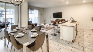 A modern kitchen with a dining area, a TV mounted on the wall, and a balcony with a view. - 4BR 3BA, Access 2 Waterparks, Private Pool, FREE Grill. Near Disney Orlando! (Davenport)