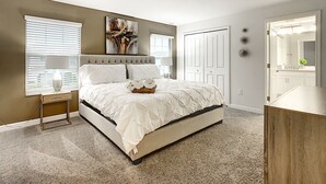 A bedroom with a bed, bedside table, lamp, artwork, and a door. - 4BR 3BA, Access 2 Waterparks, Private Pool, FREE Grill. Near Disney Orlando! (Davenport)
