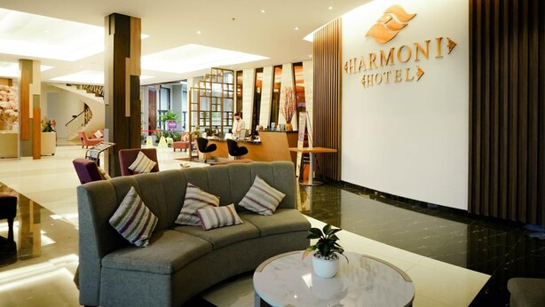 A modern hotel lobby with a reception desk, seating area, and a staircase. - Harmoni Garut (Garut)