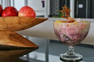 Un postre en un recipiente de vidrio, con un bol de manzanas de madera al fondo.