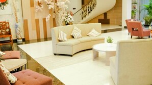 A modern lobby with a curved staircase, a sofa, a coffee table, and a pink chair. - Harmoni Garut (Garut)