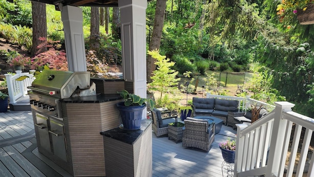 Een overdekt terras buiten, met een barbecue, zitgedeelte en potplanten.