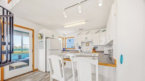 A modern kitchen with white cabinets, a central island with chairs, and a view of the outdoors. - Soundside Home w/ Private Pool, Game Room, Basketball, and Nearby Beach Access (Avon)