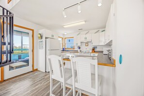 A modern kitchen with white cabinets, a central island with chairs, and a view of the outdoors.