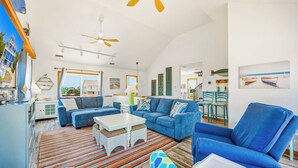 A spacious living room with a large sofa, a smaller sofa, a coffee table, and a chair. There are two ceiling fans, a window with a view, and a dining area with chairs and a table. - Soundside Home w/ Private Pool, Game Room, Basketball, and Nearby Beach Access (Avon)