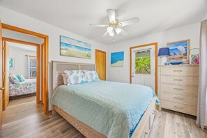 A bedroom with a bed, a ceiling fan, a dresser, and two doors leading to other rooms.