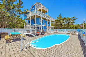 A pool with a wooden deck, lounge chairs, and a multi-level building with a balcony. - Soundside Home w/ Private Pool, Game Room, Basketball, and Nearby Beach Access (Avon)