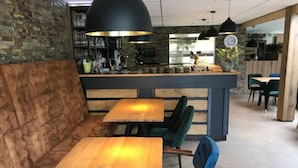 A cozy seating area with wooden tables and cushioned benches, a bar area with a counter, and a kitchen in the background. - De Brenkberg by Interhome (Schinveld)