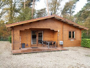 A wooden cabin with a covered patio, a table and chairs, and a window. - De Brenkberg by Interhome (Schinveld)
