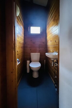Une petite salle de bain aux murs lambrissés, avec des panneaux de bois, comprenant des toilettes, une petite fenêtre et un lavabo.