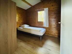 A small, single-bed room with wooden walls and a window with white curtains. - De Brenkberg by Interhome (Schinveld)