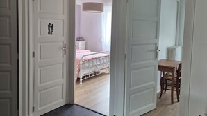 Una habitación con una cama, una mesa y una silla. Hay una puerta que da a otra estancia.