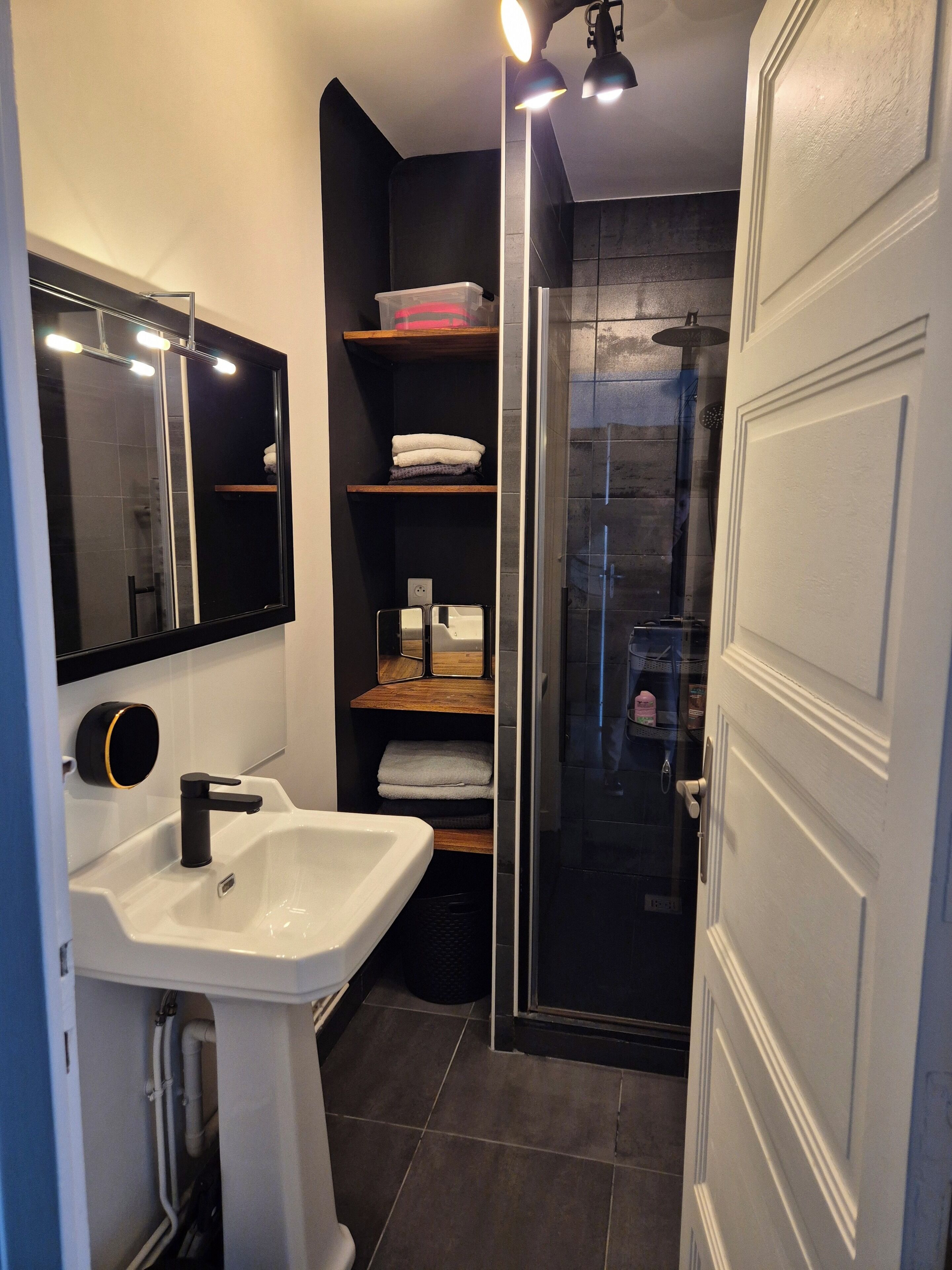 Une salle de bain moderne avec un lavabo blanc, un miroir, une cabine de douche en verre et une porte.