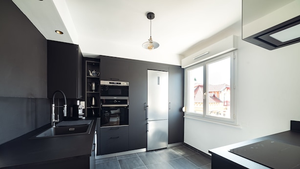 Una cocina moderna con armarios oscuros, electrodomésticos de acero inoxidable y un amplio ventanal que proporciona luz natural.